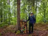 Person ved en trestamme og en fargerik vedstabel i en grønn skog.