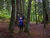 Person med løftede armer mellom trær i en tett, grønn skog.