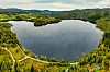 Flyfoto av en innsjø omgitt av skog, åser og en svingete vei.