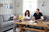 To voksne og et barn sitter rundt et trebord i en lys stue.