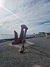 Rustent anker med kjetting på en steinete strand under en skyet himmel.