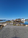 Asfaltvei gjennom steinete kystlandskap mot hvite hus ved blått sjøvann.