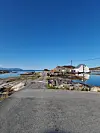 Asfaltvei gjennom steinete kystlandskap mot hvite hus ved blått sjøvann.