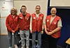 Fire personer i røde vester står sammen i et møterom.