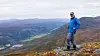 Fjellvandrer med staver på en fjellkam over et vidstrakt dalandskap.