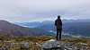 Person på en fjelltopp med utsikt over blå fjell, daler og høstfarget terreng.