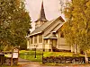 Hvit trekirke med spir omgitt av gule høsttrær og steingjerde.