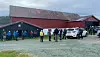 Mennesker og kjøretøy samlet utenfor en stor rød låve i et landlig område.