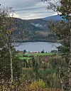 Innsjø og gårder omgitt av høstskog og fjell sett mellom trær.