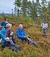 Fire turgåere hviler på en skogkledd åsside med turutstyr rundt seg.