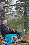 Turgåer sitter ved et tre med sekk, turutstyr og to hunder i skogsterreng.