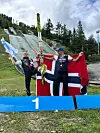 To personer med norsk flagg og ski feirer foran en hoppbakke.
