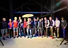 Gruppe mennesker står på rekke i et mørkt arrangementsområde med scenelys.