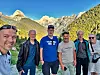 Seks personer poserer foran høye fjell og en grønn dal i solskinn.