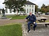 En mann sitter på en benk i en park foran en hvit historisk bygning.