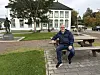 En mann sitter på en benk i en park foran en hvit historisk bygning.