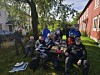 Gruppe mennesker samlet rundt et bord i en grønn hage mellom trehus.