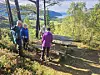 Turgruppe i fargerike klær på skogssti med fjell og vann i bakgrunnen.