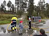 Barn øver med vannslanger sammen med en instruktør på en våt skogsvei.