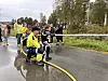Mannskap i gule verneklær håndterer en vannslange på en regnvåt vei.