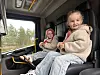 To barn sitter i et lastebilførerhus, med skog utenfor vinduet.