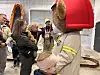 Barn i brannmannskapets utstyr foran en brannbil mens voksne følger med.