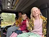 Smilende barn sitter på seter inne i en buss med skog synlig gjennom vinduet.