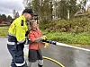 Voksen og barn bruker en vannslange på en våt vei i skogen.