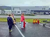 Tre barn på en våt parkeringsplass foran en butikkbygning.