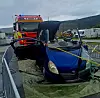 Skadet blå personbil bak avsperring, med utrykningskjøretøy i bakgrunnen.