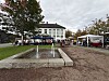 Utendørs marked med telt og boder ved en fontene og en hvit bygning.