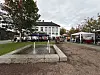 Utendørs marked med telt og boder ved en fontene og en hvit bygning.