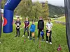 Barn står samlet på en gresslette med flagg på bakken, kjegler og fjell i bakgrunnen.