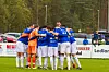 Fotballag i blå drakter samles i ring på en gressbane før kamp.
