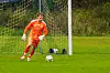 Fotballmålvakt i oransje drakt foran målet, med ballen på gresset.