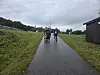 To personer på en våt gang- og sykkelvei med gressbakker og overskyet vær.