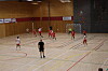 Håndballspillere i rødt og hvitt i aksjon i en innendørs idrettshall.