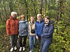 Fem blide turkledde damer står samlet på en skogssti blant trær og høstløv.
