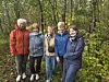Fem blide turkledde damer står samlet på en skogssti blant trær og høstløv.