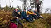 Gruppe personer sitter samlet i skogen blant høstfargede busker og trær.