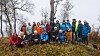 Stor gruppe mennesker i friluftsklær poserer på en skogkledd høyde.