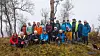 Stor gruppe mennesker i friluftsklær poserer på en skogkledd høyde.