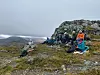 En gruppe turgåere sitter ved en steinformasjon på en karrig fjellrygg.