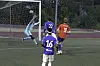 Målvakt i turkis drakt kaster seg foran mål mens fotballspillere i blått og rødt følger spillet.