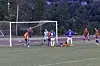 Fotballspillere foran mål på en kunstgressbane, med en spiller liggende på bakken.