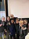 Gruppe barn og en voksen som smiler sammen i et lyst innendørsrom.