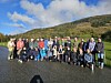 Gruppe turgåere poserer foran en skogkledd ås under en blå himmel.