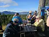 Ei gruppe turkledde personer ved et rasteplasspord med innsjø og fjell i bakgrunnen.