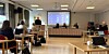 Møte med deltakere, bærbare datamaskiner og presentasjonsskjerm i et konferanserom.