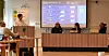 Paneldeltakere sitter ved et bord foran en stor digital presentasjon.